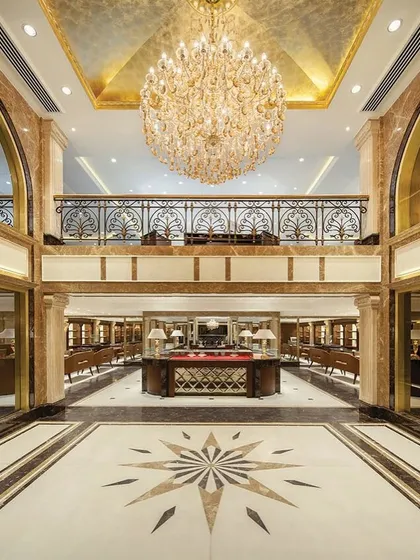 The interior of Anand Jewels is defined by its grand scale, featuring a double-height atrium and a sweeping staircase. The flooring, a combination of Golden Empress stone and white marble, creates a radial pattern that adds to the sense of opulence.