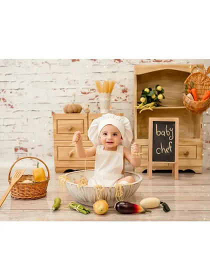 A happy little chef playing with his ingredients. The rustic brick background and wooden furniture complete the charming kitchen scene.