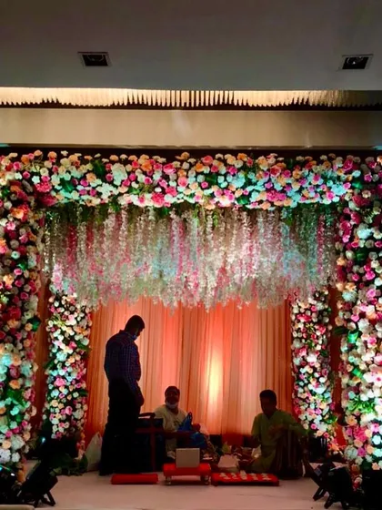 Here is a pastel-themed mandap fully decorated with a mix of colorful flowers. The design features hanging strings of white flowers that create a delicate curtain effect, perfect for a modern and romantic wedding ceremony.