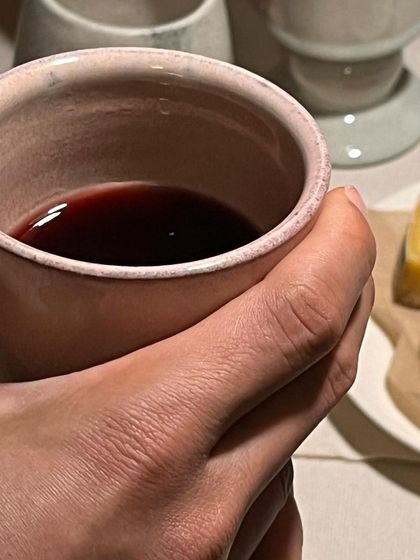 A hand holding one of the goblets, filled with red wine. The form is designed to be comfortable to hold, enhancing the ritual of drinking.