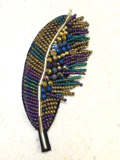 A detailed look at the iridescent beaded feather patch. The intricate beadwork catches the light beautifully, making it a stunning accessory for clothing, hats, or bags.