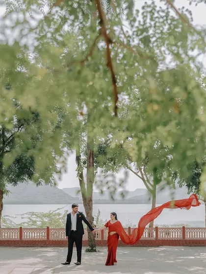 A dramatic, cinematic shot with the bride's red saree flowing in the wind, creating a stunning visual against the natural backdrop.