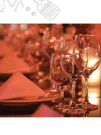 A close-up of a perfectly set table, glowing under the warm lights of an evening event. The clean lines of the folded napkin, the polished wine glasses, and the ambient lighting all contribute to an atmosphere of refined sophistication.