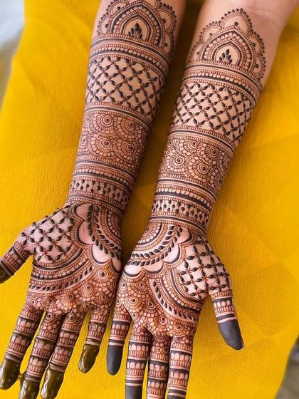 Full bridal mehandi with heavy, intricate patterns covering both hands and extending up the arms. This design uses traditional check patterns, floral motifs, and detailed finger work for a classic bridal look.