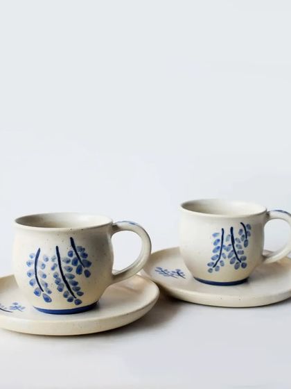 A charming hand-painted tea or coffee cup and saucer set. The delicate blue wisteria-like design adds a touch of artisanal elegance to your daily ritual.