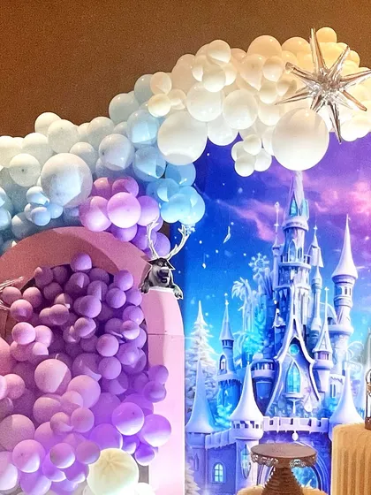 A detailed view of the balloon artistry, with a mix of purple, blue, and white balloons creating a cascading effect next to the magnificent castle backdrop.