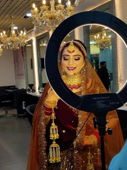 A happy bride posing with the ring light. Her smile says it all. The makeup features a classic red lip and golden-hued eyeshadow, a timeless combination for Indian brides.