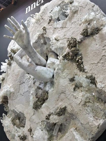 A powerful sculpture by Maria Molaei of hands breaking through a stone-like surface.