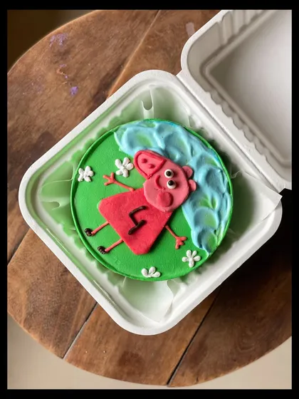 A top-down view of the Peppa Pig bento cake, showing Peppa enjoying a muddy puddle made of buttercream.