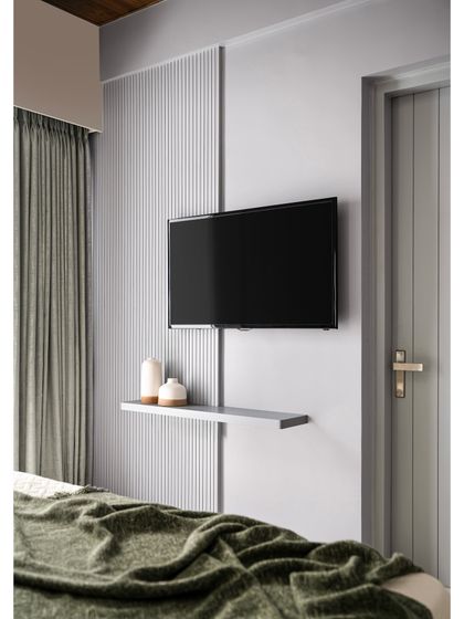 A minimalist TV unit solution for a bedroom. This design features a simple floating shelf and a vertical fluted panel that conceals wiring, maintaining a clean and uncluttered look.
