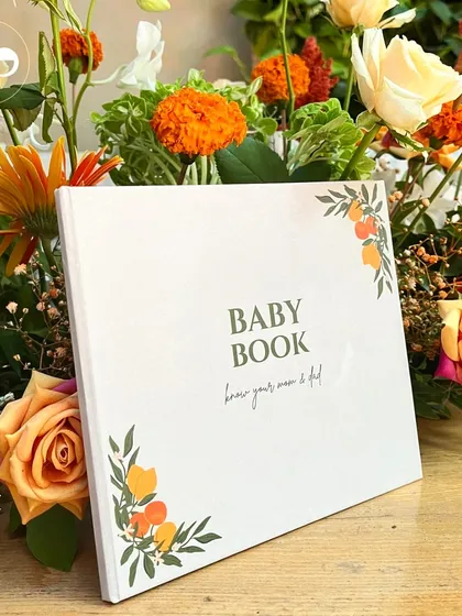 A custom "Baby Book" for guests to sign, set against a backdrop of vibrant orange flowers. This is a wonderful way to create a lasting memory of the day.