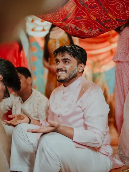 The groom enjoying the Haldi rituals, seated under a traditional decorated cloth. We ensure that even the most candid moments are beautifully framed.