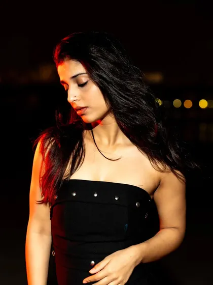 A soft, downward glance lit by flash. This pose creates a quiet, contemplative mood amidst the darkness.