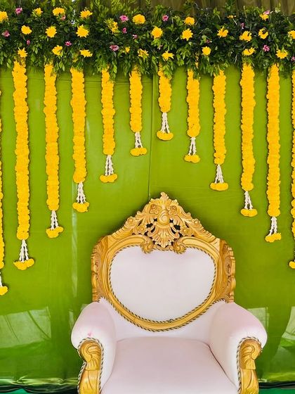A simple and budget-friendly Seemantham setup. The decor features a green backdrop with an arch of yellow flowers and hanging marigold garlands.