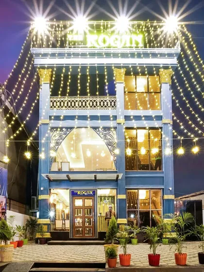The grand exterior of The Rogan restaurant at night, adorned with festive fairy lights. The multi-story building has a striking blue facade with gold accents, making it a landmark in the area.