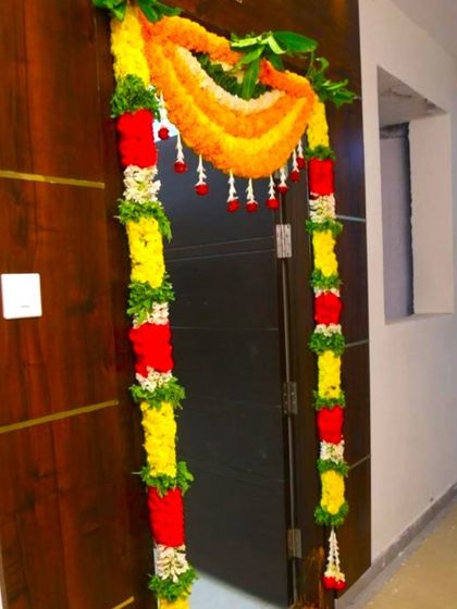 A flower decoration for a housewarming at home. The door is framed with garlands of red and yellow flowers with green leaf accents.