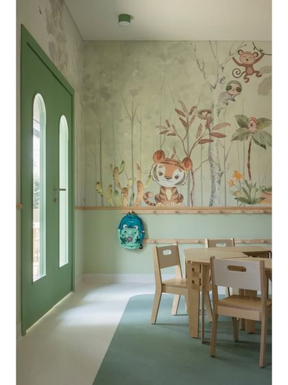 Welcome to the forest-themed classroom for LKG students. A friendly tiger peeks out from the custom wallpaper, set against a backdrop of soft green tones. The modular birch ply furniture is both beautiful and functional.