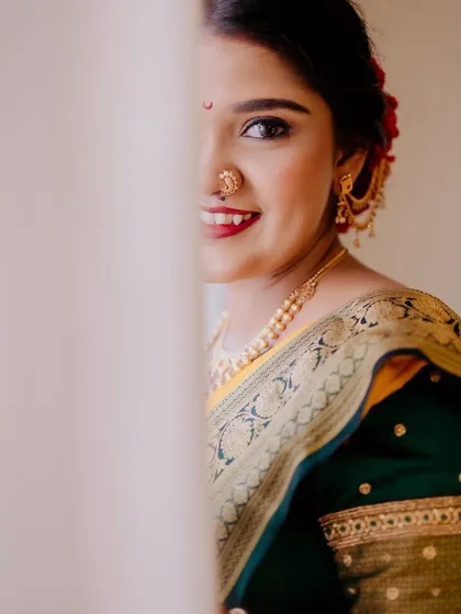A peek-a-boo shot of a beautiful bride. The makeup is classic, with a bold red lip and defined eyes that perfectly match her traditional attire.