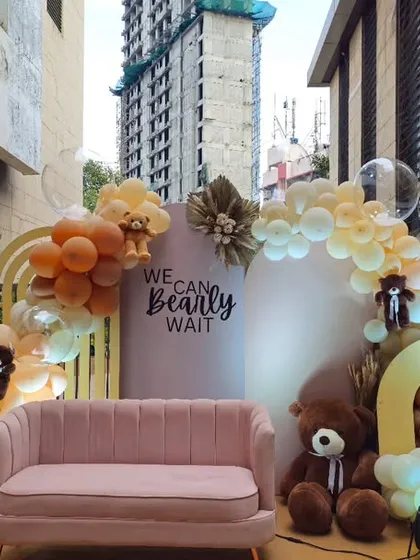 An outdoor teddy bear setup with a "We Can Bearly Wait" theme, featuring a comfortable pink sofa for photos and balloon arches in earthy tones.