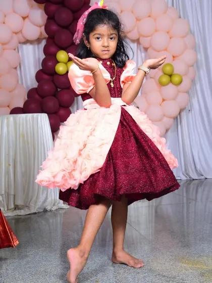 Look at this little one striking a pose! I designed this custom birthday frock with a sparkling maroon skirt and fluffy pink floral details just for her special day. Seeing her so happy and confident is the best reward.