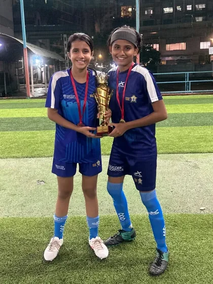 Two teammates share the joy of victory, holding the championship trophy together. This image embodies the teamwork and friendship we foster in our U17 girls squad.