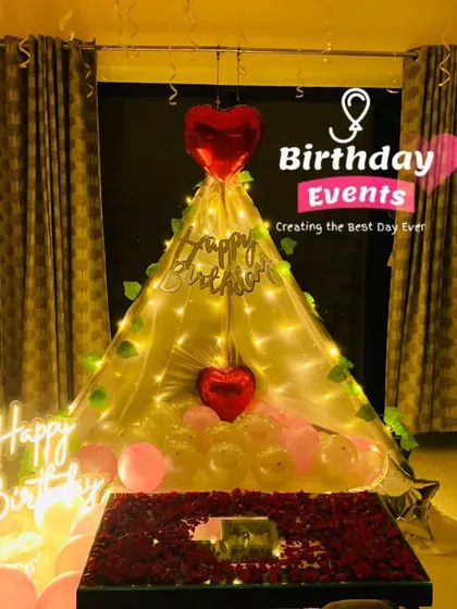 Create a cozy and romantic birthday surprise right at home. This setup features a beautiful canopy tent filled with balloons and wrapped in fairy lights, with a dedicated table for cake and gifts, all personalized for the special day.