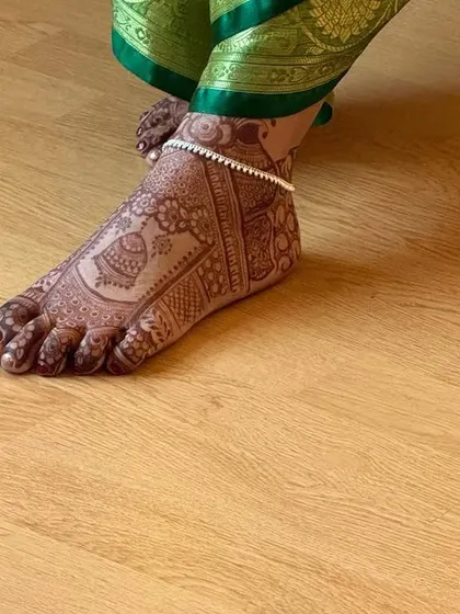 A side view of a bridal foot mehendi, showing the elegant design and how it looks with a traditional payal (anklet).