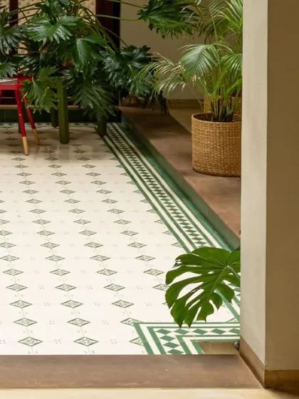 The patterned cement tile floor of a courtyard, surrounded by lush indoor plants. This space is the heart of the home, bringing a touch of the garden indoors.