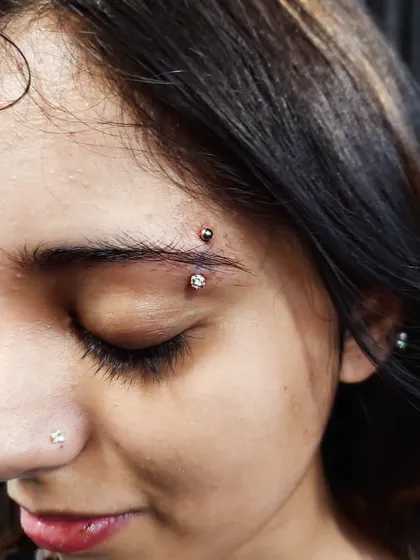 A vertical eyebrow piercing featuring a dual-jewel barbell. This type of surface piercing adds a unique edge to your look, and I ensure proper placement for better healing.