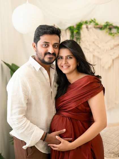 A bright and happy couple's portrait. The expecting mother and her partner are all smiles in a naturally lit room with bohemian decor, creating a relaxed and joyful atmosphere.