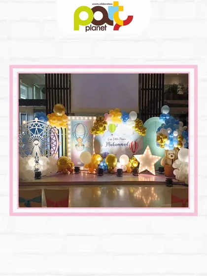 A beautiful stage setup for a hot air balloon themed party, complete with a Ferris wheel prop, marquee lights, and soft, cloud-like decor.