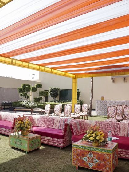 This Haldi celebration combined traditional colors with modern comfort. We used vibrant pink sofas with printed covers and colorful hand-painted tables, all set under a bright orange and white striped canopy for a festive feel.