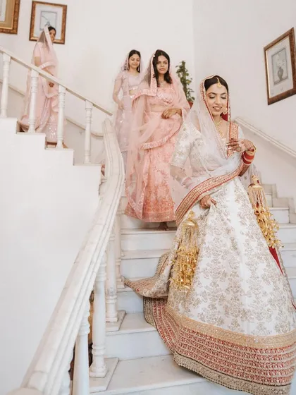 The bride, followed by her bridesmaids, makes her way down a grand white marble staircase.