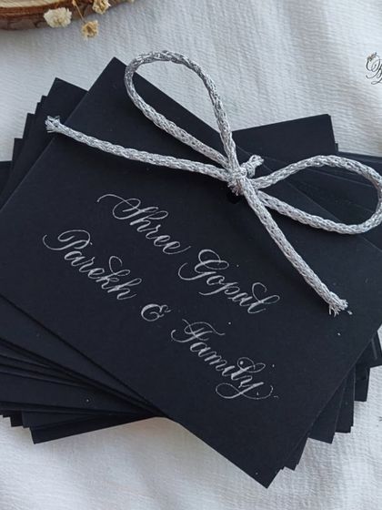 Guest name tags for the 25th-anniversary celebration, handwritten in silver ink on black cardstock to match the elegant black-and-silver theme of the event.