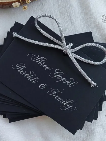 Guest name tags for the 25th-anniversary celebration, handwritten in silver ink on black cardstock to match the elegant black-and-silver theme of the event.