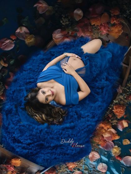 A dreamy, artistic overhead shot of a mom-to-be in a royal blue gown, lying in a boat surrounded by flowers. This is a highly creative and unique concept for a maternity shoot.