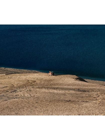 A lone vehicle stands on the barren shore of Tso Moriri, providing a sense of scale to the vast, empty landscape.