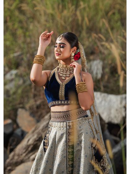 An outdoor bridal shoot capturing a serene and elegant moment. The natural setting complements the traditional lehenga, and the soft lighting highlights the delicate details of the fabric and embroidery.