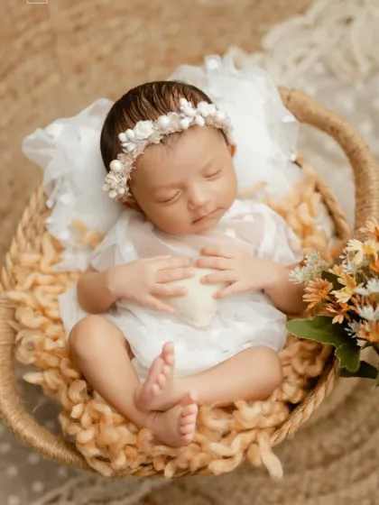 A peaceful newborn in a basket, dressed in white with a matching floral headband.