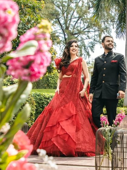 A beautiful outdoor shot of the couple. The bride's red engagement lehenga is complemented by a glamorous yet elegant makeup look.