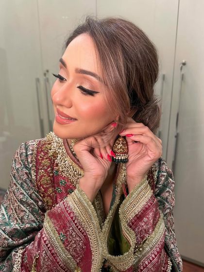 A candid moment of the guest putting on her earrings, showcasing the flawless makeup and the beautiful side profile.