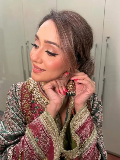 A candid moment of the guest putting on her earrings, showcasing the flawless makeup and the beautiful side profile.