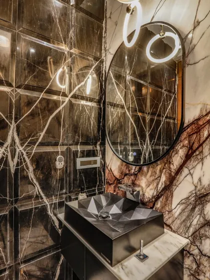 In this powder room, we used dramatic, book-matched marble and beveled wall tiles to create an immersive experience. The geometric basin and modern lighting add a contemporary edge, proving that even small spaces can make a powerful statement.