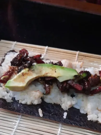 The process of rolling a homemade veg sushi roll on a bamboo mat, ensuring all the fresh ingredients are packed in tightly.