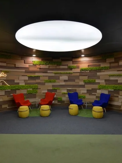 For Globant's office, we did away with the traditional reception desk entirely. Instead, we created a welcoming lounge with a moss and wood-paneled wall, neon signage, and colorful seating.
