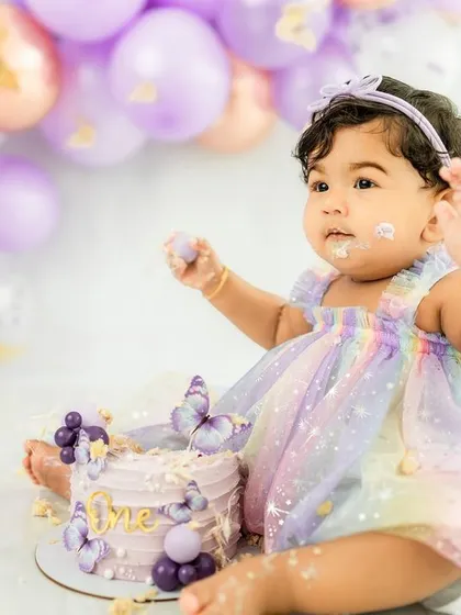 The aftermath of a delightful cake smash, with frosting on her fingers and a happy, curious expression.