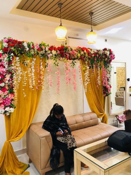 An elegant backdrop created inside a home for a small function. This setup features yellow curtains draped with a thick garland of artificial flowers, perfect for photos.