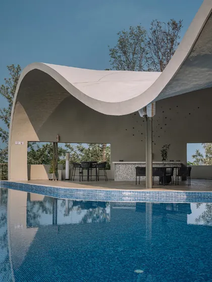 The structure of the Aqua Pool & Spa provides a covered poolside lounge and bar area, with large openings that frame the surrounding trees and hills.