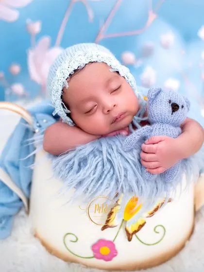 A sweet newborn holding a tiny blue teddy bear, posed in a watering can prop for a whimsical garden-themed shoot.