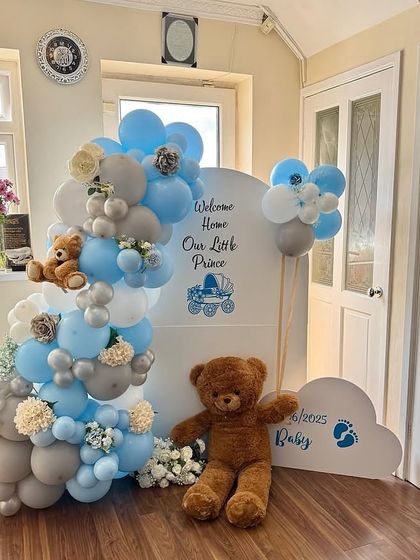 A full view of the 'Welcome Home Our Little Prince' setup, showing the arrangement of the backdrops, balloon garlands, and the large teddy bear.